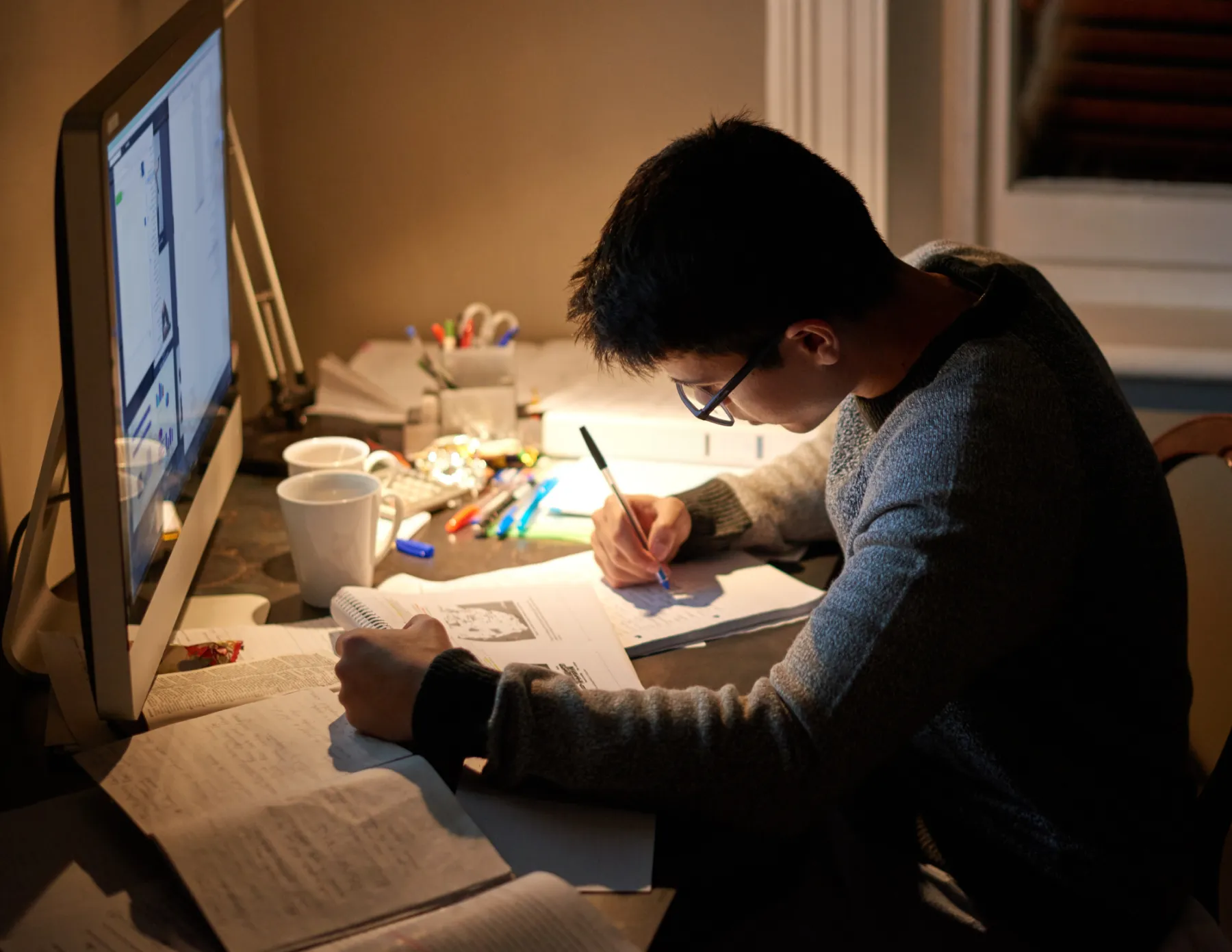 Studerende jongen met pen en papier achter zijn laptop