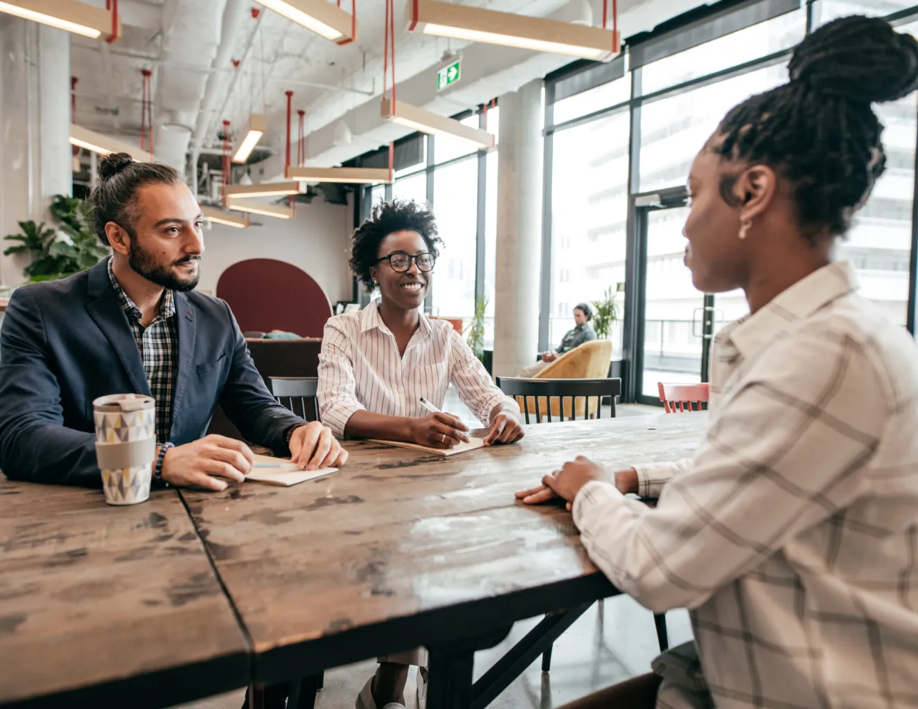 Vrouw in sollicitatiegesprek met 2 anderen, aan tafel met notities